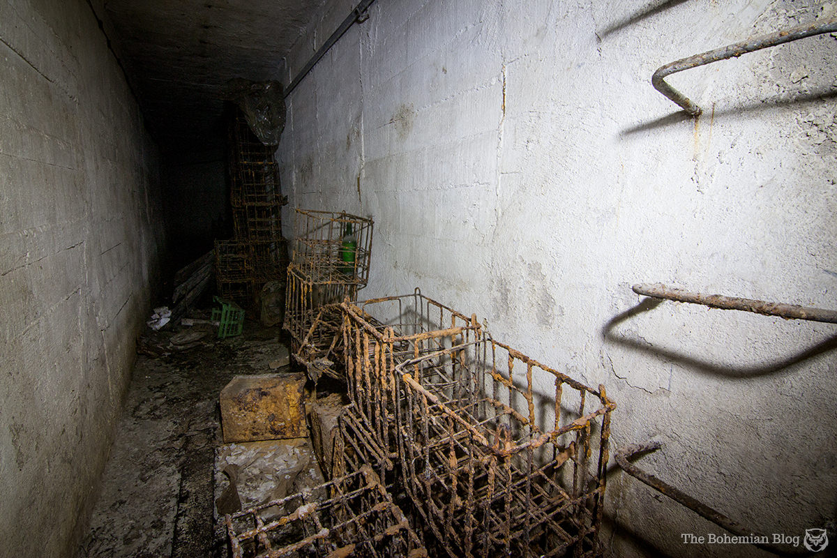 In a back corridor, wire crates lie rusting beside the ladder to a manhole in the street above.